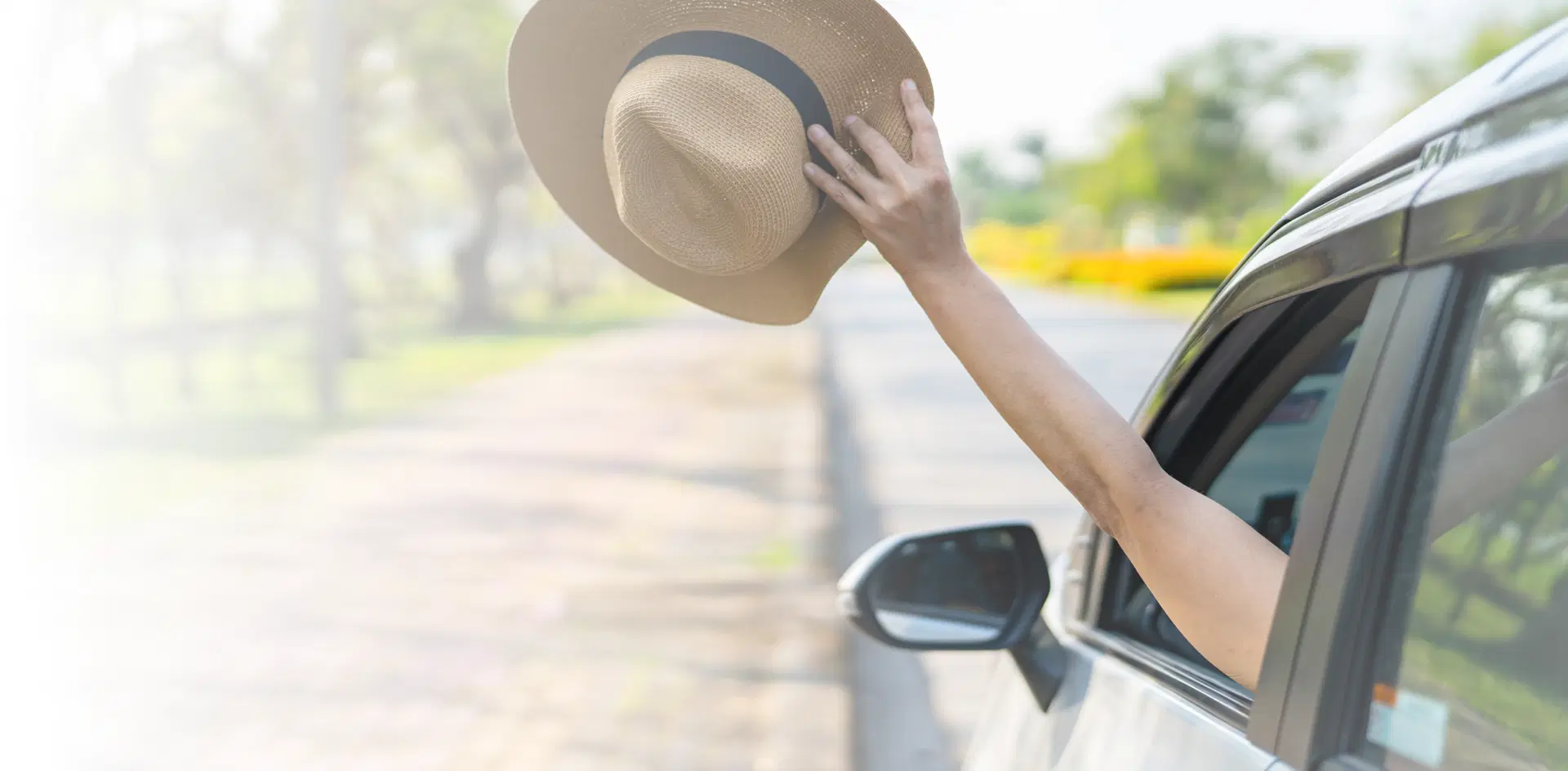Girl holding a white woven hat and reaching it out of the car.
