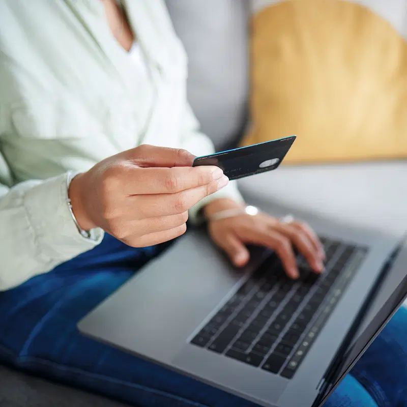 Close-up of a person typing on a computer for internet use while holding a credit card.